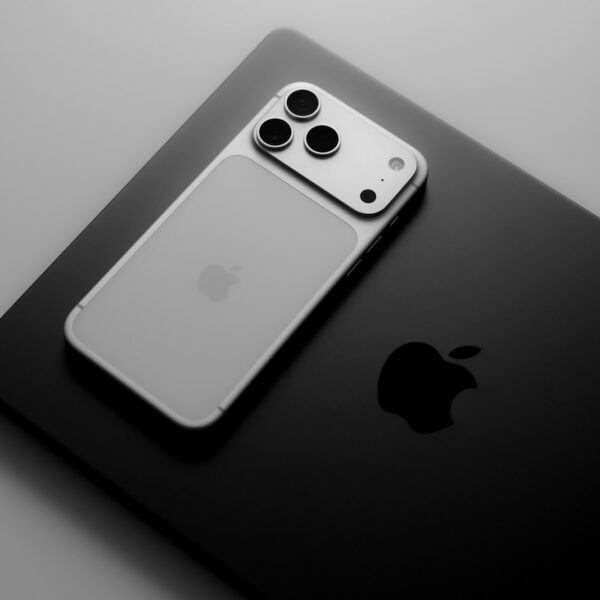 Smartphone resting on laptop with apple logos.